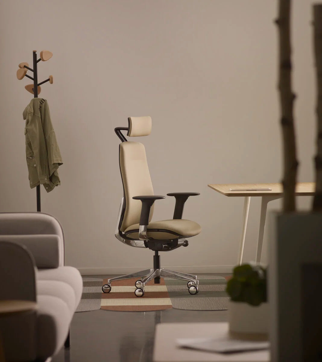 bureau avec un chaise ergonomique de couleur beige et un canapé gris ainsi qu'un porte manteaux en arrière plan